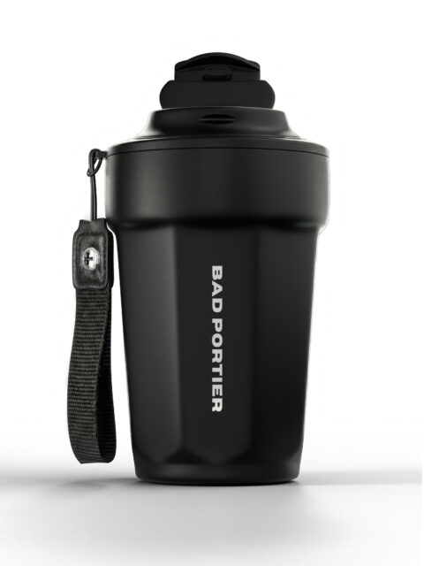 Matte black BAD PORTIER "Solid" Thermal Cup in faceted stainless steel with a flip-lid and a woven wrist strap attached by a vegan-leather patch and single screw rivet. Laser-engraved vertical logo on the front.